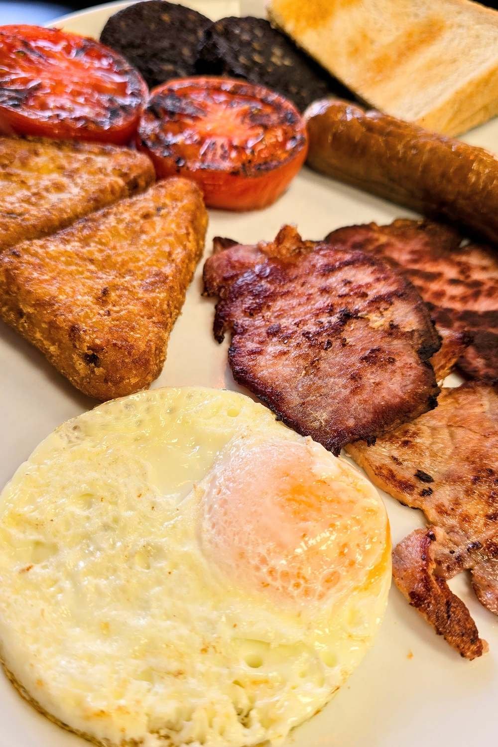 Plato de full English breakfast con huevo frito, bacon, salchicha, morcilla, tomate asado, hash brown y tostada